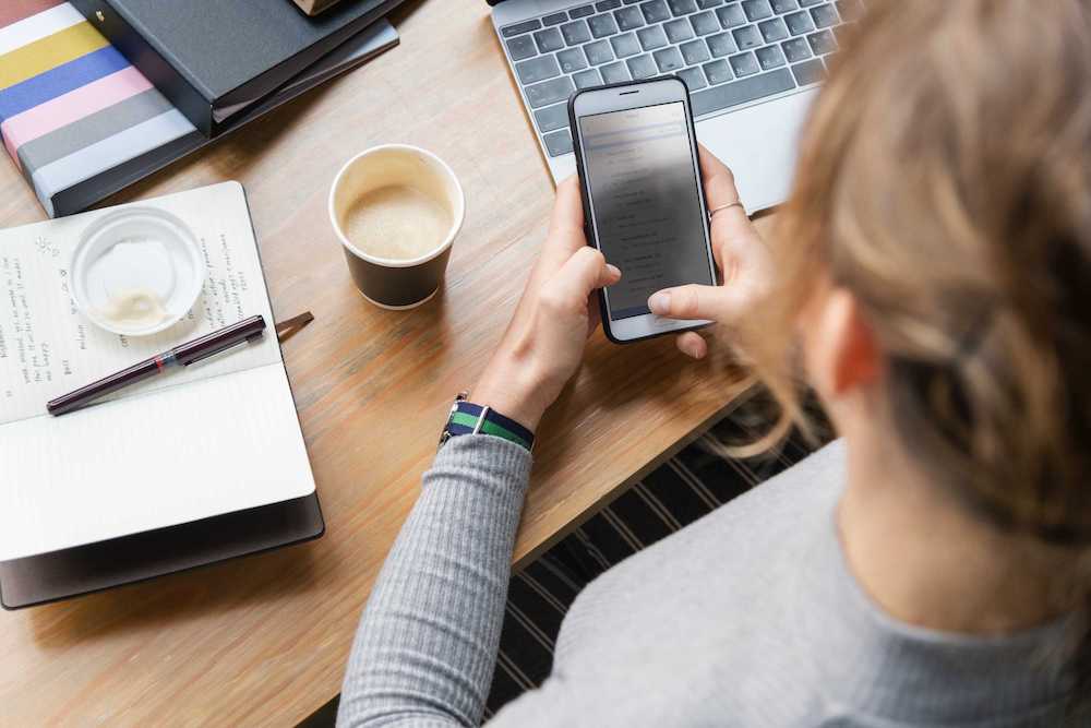 Woman interacting with mobile phone with coffee and notebook on table